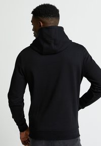 Felpa nera con cappuccio, dal tessuto morbido, maniche lunghe e vestibilità comoda. Presenta un collo alto e polsini a costine. Design semplice, senza grafiche.