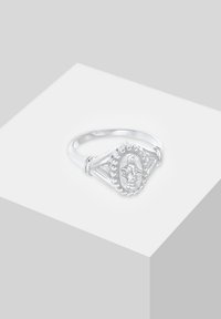 Anneau en argent présentant une figure religieuse ovale entourée de petites perles sur une bande fendue, exposé sur un piédestal blanc.