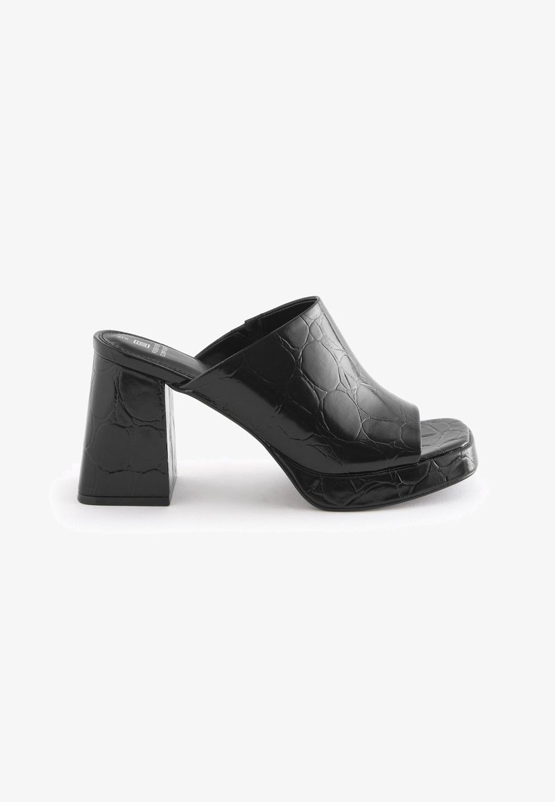 Mule noire à talon haut avec une large bride à motif crocodile, talon bloc et bout ouvert, présentée sur fond blanc.