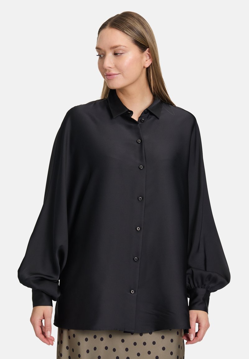 Camicia nera in satin con colletto, maniche a palloncino oversize e taglio dritto, abbinata a una gonna a pois.