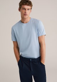 Világoskék pamut póló kerek nyakkivágással és rövid ujjúval, sötét tengerészkék szabott nadrággal párosítva, amely gombos záródással rendelkezik.