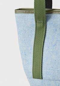 Τσάντα από γαλάζιο υφασμάτινο ύφασμα με πράσινο πλεγμένο λουράκι και ελιάς πράσινα ραμμένα περιθώρια κατά μήκος της πάνω ακμής.