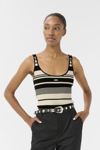 Débardeur tricoté avec des rayures horizontales noires et crème, encolure dégagée et bretelles larges. Associé à un pantalon noir taille haute et une ceinture cloutée.