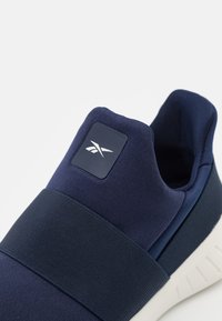 Námořnická sportovní obuv s textilním svrškem, elastickou páskou a strukturovanou podrážkou. Na límci je logo.