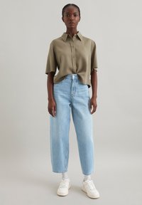 Olivgrünes kurzärmeliges Hemd mit Knopfleiste, kombiniert mit hellblauen, hoch taillierten, weiten Jeans und weißen Sneakern.
