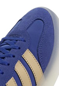 Modré semišové svršky s béžovými koženými pruhy, texturované akcenty a modrými šňůrkami. Zaoblená špička a průhledná gumová podrážka.