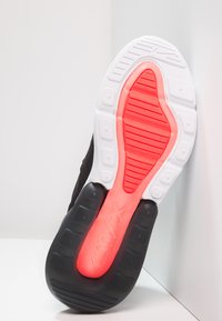 Suola di scarpa atletica nera con una sezione esterna bianca, caratterizzata da un'area di ammortizzazione rossa prominente, testurizzata con scanalature e sezioni sollevate.