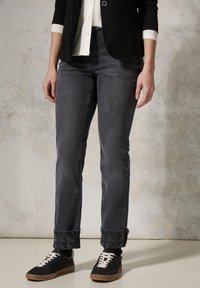Jeans de mezclilla gris oscuro, con un corte recto, puños enrollados con detalles estampados, combinados con zapatillas negras y una camisa blanca.