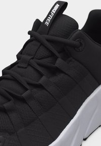 Κοντινό πλάνο μαύρου αθλητικού παπουτσιού με επάνω μέρος από δίχτυ, ενσωματωμένα κορδόνια, θηλιά έλξης με την ετικέτα "NIKE FREE" και λευκή σόλα με υφή.