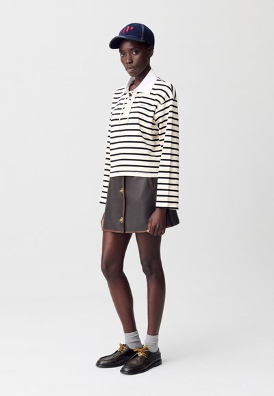 Camicia a maniche lunghe a righe in crema e nero, abbinata a una gonna di pelle marrone con bottoni dorati, calze grigie e scarpe con lacci nere.