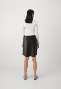 Falda de cuero negro con una textura suave y una silueta recta, combinada con una blusa ajustada de manga larga blanca y zapatos de colores claros.