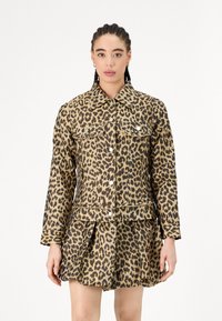 Denim jakna z leopardjim tiskom, s pritisnimi gumbi, dvema žepoma na prsih in dolgimi rokavi, v kombinaciji z usklajeno plisirano krilo.