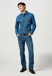 Blå denimjacka och jeans med en klassisk design, knappfront, bröstfickor och en ren finish. Bärs med svarta ankelskor.