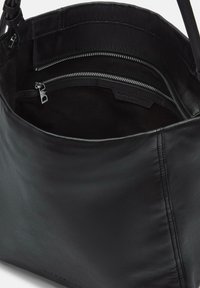 Czarna skórzana torebka z otwartym wierzchem, pokazująca kieszeń na zamek błyskawiczny w środku oraz gładką powierzchnię na zewnątrz.