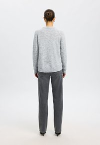 Szürke kötött pulóver kerek nyakkal, szürke egyenes szárú farmerrel párosítva. Texturált anyag, finom részletek és szabott fazon.