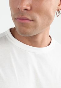 Bílý crewneck tričko s hladkou texturou, s příjemným ribbed výstřihem a jemnými švy na rameni.
