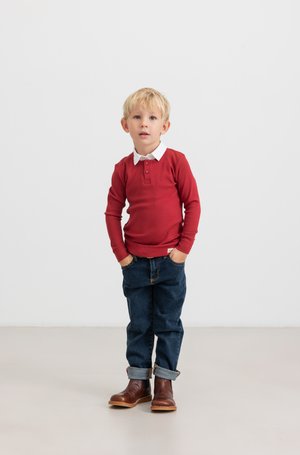 Rode geribbelde lange mouw shirt met witte kraag, gecombineerd met opgerolde donkerblauwe jeans en bruine laarzen. Gladde textuur, casual pasvorm.