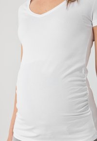 Balts īsām piedurknēm V-veida kakla krekls, kas izgatavots no mīkstas kokvilnas, ar sānu rušēšanu, lai piešķirtu papildu apjomu un pieguļošu izskatu. Gluda tekstūra.