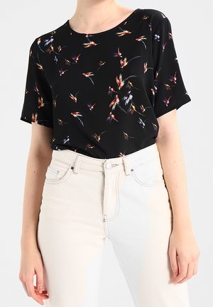 Sort kortærmet top med blomstermønster i levende farver, parret med lysfarvede højtaljede jeans. Glat stofstruktur.