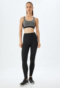 Zwarte leggings gecombineerd met een grijze sportbeha met een gestructureerd patroon. De outfit wordt aangevuld met zwarte sportschoenen.