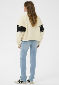 Sweatshirt court crème avec des rayures noires, associé à un jean skinny bleu clair et des baskets avec accents noirs. Texture lisse sur l'ensemble.