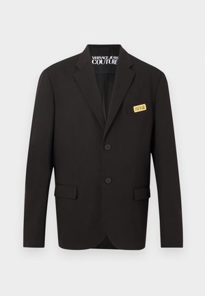 Blazer nero sartoriale con due bottoni anteriori, tasche con pattina e etichetta dorata "Versace Jeans Couture" sulla tasca al petto.