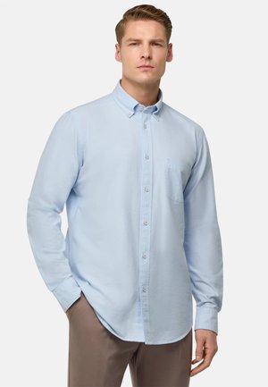 Chemise bleu clair à manches longues, avec une poche sur le devant et un ourlet arrondi. Fabriquée en tissu doux avec une texture lisse.
