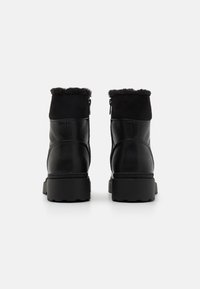 Black ankle boots featuring smooth leather and suede materials, a plush fur lining at the top, a sturdy rubber sole, and zip closure.