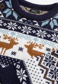 Pull tricot bleu marine, blanc et marron avec motifs de rennes et flocons de neige, col côtelé, et étiquette « NEXT Fabriqué au Bangladesh ».