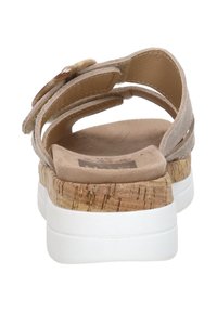 Beige suede sandal with a cork wedge heel and white rubber sole. Velcro strap and decorative button detail on the back.