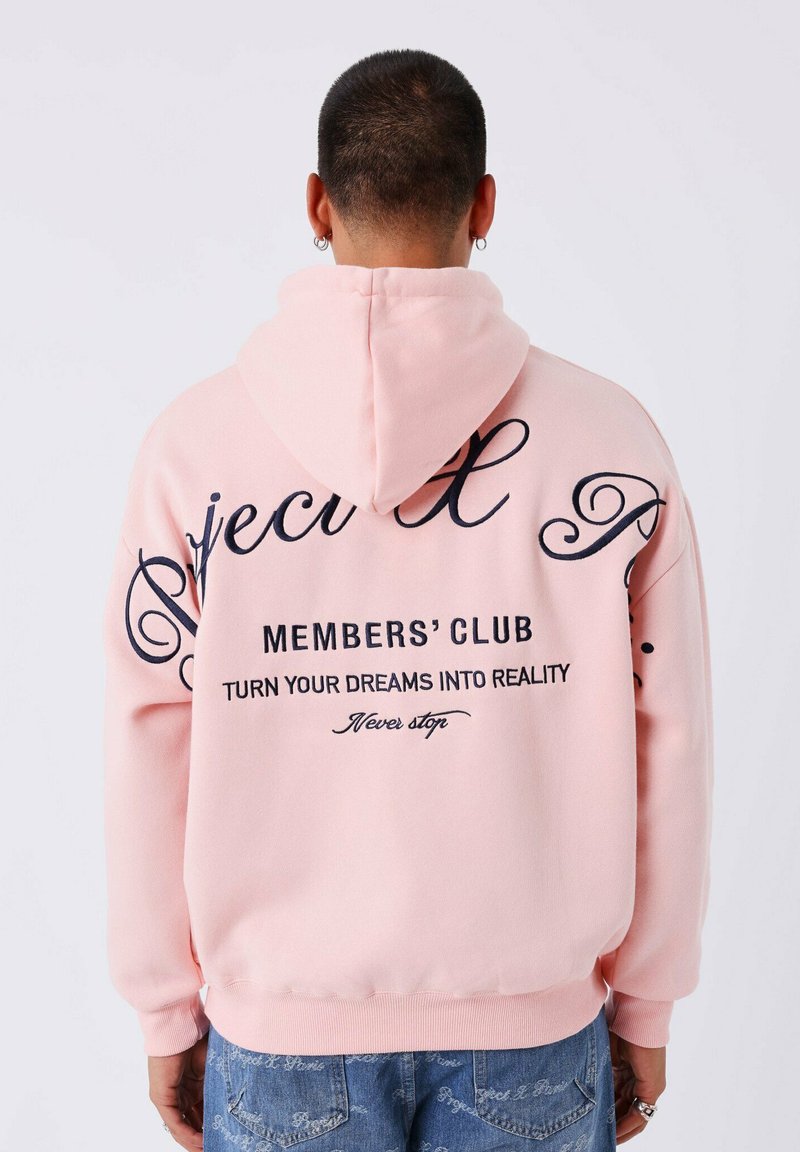 Roze hoodie met een trekkoordkap, met grote zwarte tekst op de achterkant: "MEMBERS' CLUB," "TURN YOUR DREAMS INTO REALITY," en decoratieve schrift.