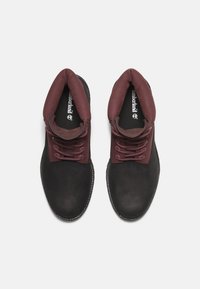 Bottines noires et bourgognes avec un dessus en cuir texturé, un col rembourré et des lacets assortis ; dotées d'une semelle en caoutchouc robuste.