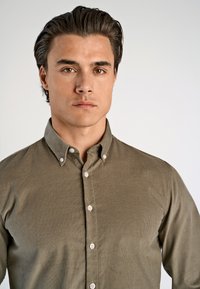 Olijfgroene button-up shirt van gebreide stof, met een klassieke kraag en witte knopen aan de voorkant.
