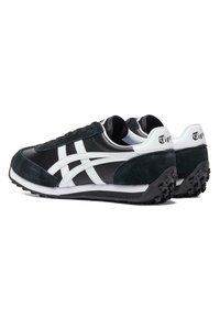 Para czarno-białych niskich trampek z teksturowaną podeszwą i białymi paskami po bokach, widocznych z tyłu pod kątem.