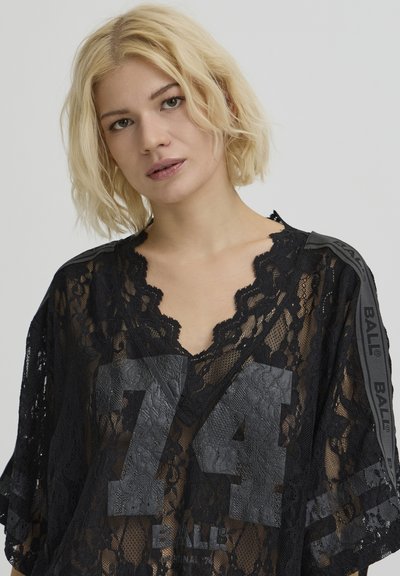 Haut noir en dentelle avec un col festonné, une coupe oversize et un grand "74" imprimé en matière texturée sur le devant. Agrémenté d'une touche de branding.