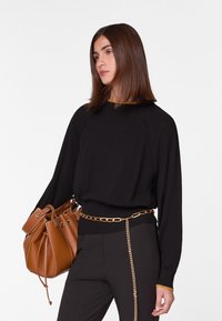 Zwarte gebreide trui met een gele halslijn, gedragen met zwarte broeken. Een bruin leren emmerzak en geaccentueerd met een gouden kettingriem.