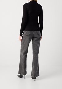 Schwarzes, geripptes Langarmshirt mit horizontalen Streifen, kombiniert mit weit geschnittenen grauen Jeans mit Taschen-Details und rohem Saum, getragen mit schwarzen Absatzschuhen.