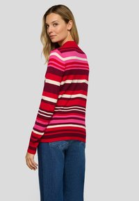 Roter Strickpullover mit horizontalen Streifen in Pink, Lila und Creme, mit langen Ärmeln und einem gerippten Kragen. Dazu getragen mit Jeans.