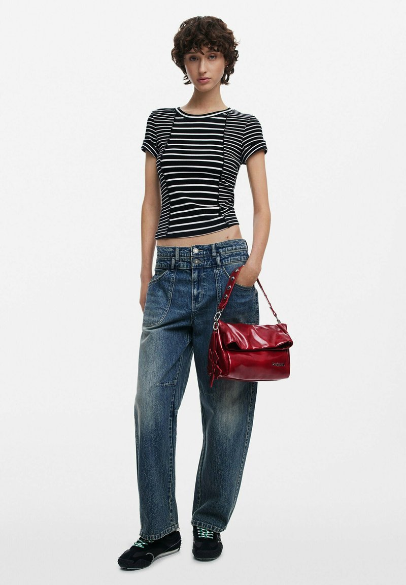 Gestreiftes schwarzes und weißes enges Oberteil kombiniert mit lockeren blauen Denim-Jeans. Das Modell hält eine glanzvolle rote Handtasche mit einem runden Deckel und einem Riemen.