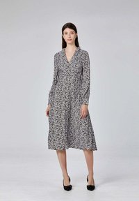 Robe à imprimé floral noir et blanc avec des manches longues, un décolleté en V et une jupe fluide, associée à des chaussures noires. Texture de tissu lisse.