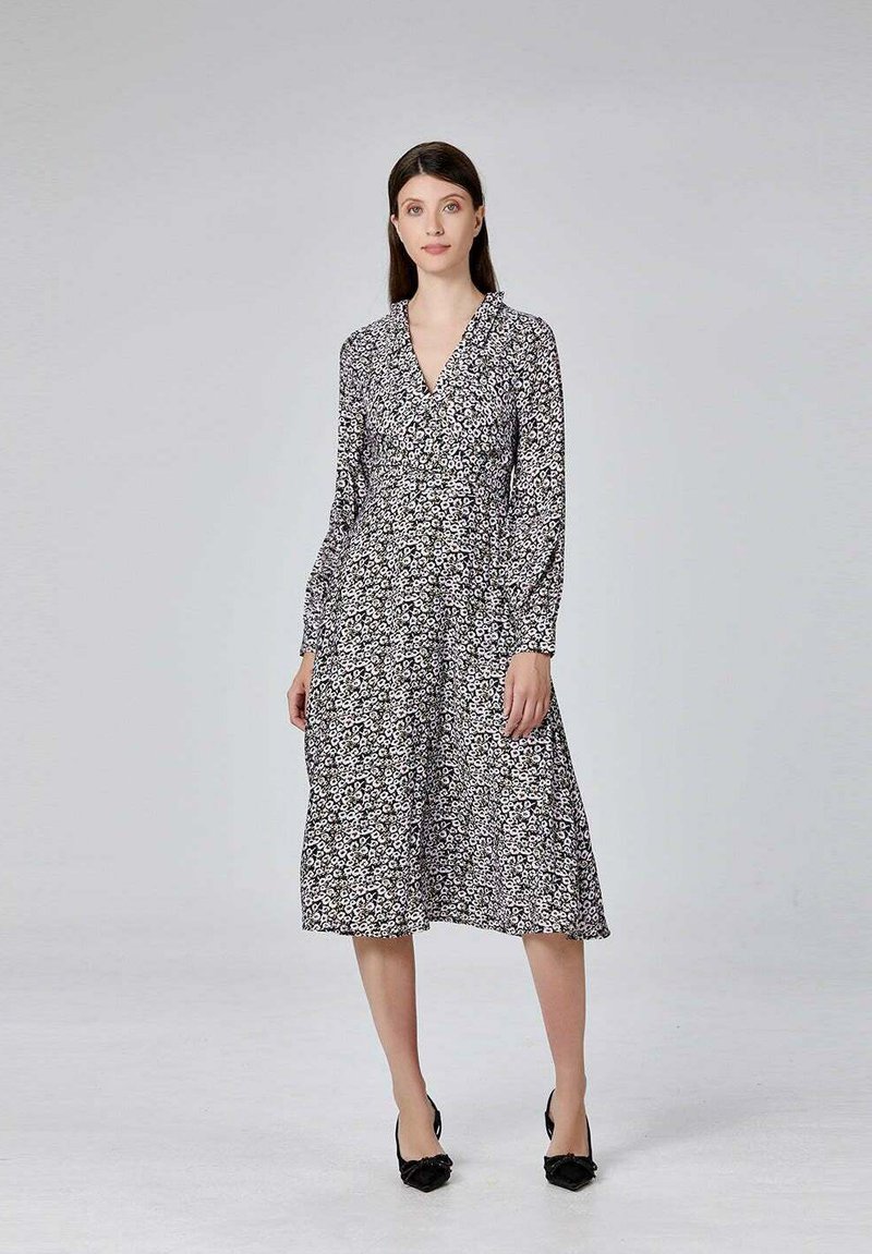Robe à imprimé floral noir et blanc avec des manches longues, un décolleté en V et une jupe fluide, associée à des chaussures noires. Texture de tissu lisse.