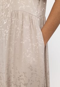 Abito beige chiaro con un delicato motivo texture, raccolto in vita con tasche laterali. Tessuto morbido con una caduta fluida.