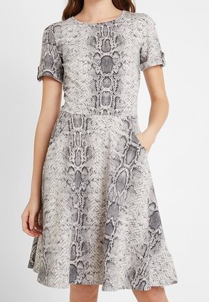 Mujer vistiendo un vestido de manga corta, longitud hasta la rodilla, con patrón de piel de serpiente en gris y negro y bolsillos laterales.