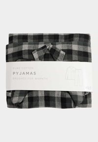 Pijamas de algodón puro en un patrón de cuadros en negro y gris, empaquetados con una etiqueta blanca que detalla las instrucciones de cuidado y el diseño.
