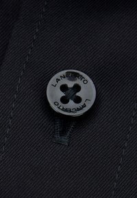 Czarny guzik z czterema otworami, wygrawerowany napisem „LANCERTO”, przymocowany do ciemnej tkaniny z widocznym szwem i gładką fakturą.