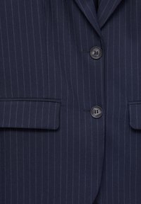 Veste de costume bleu marine à fines rayures, avec deux poches à rabat à l'avant et deux boutons noirs fermés au centre.