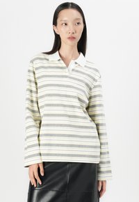 Long-sleeve polo shirt with yellow, gray, and white stripes. Features a white collar and soft cotton material, worn with a black leather skirt.