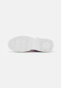 Semelle de chaussure blanche avec des motifs en forme de flammes et une zone circulaire pour le logo, présentée sur un fond clair uni.