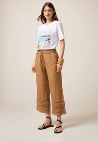 T-shirt blanc avec un design graphique coloré, associé à un pantalon court ample beige avec des accents brodés et une taille élastique.