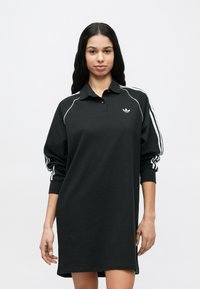 Μαύρο φόρεμα πόλο με μακριά μανίκια, λευκές ρίγες διακόσμησης και μικρό λογότυπο στο στήθος. Κατασκευασμένο από μαλακό, διαπνέον ύφασμα.